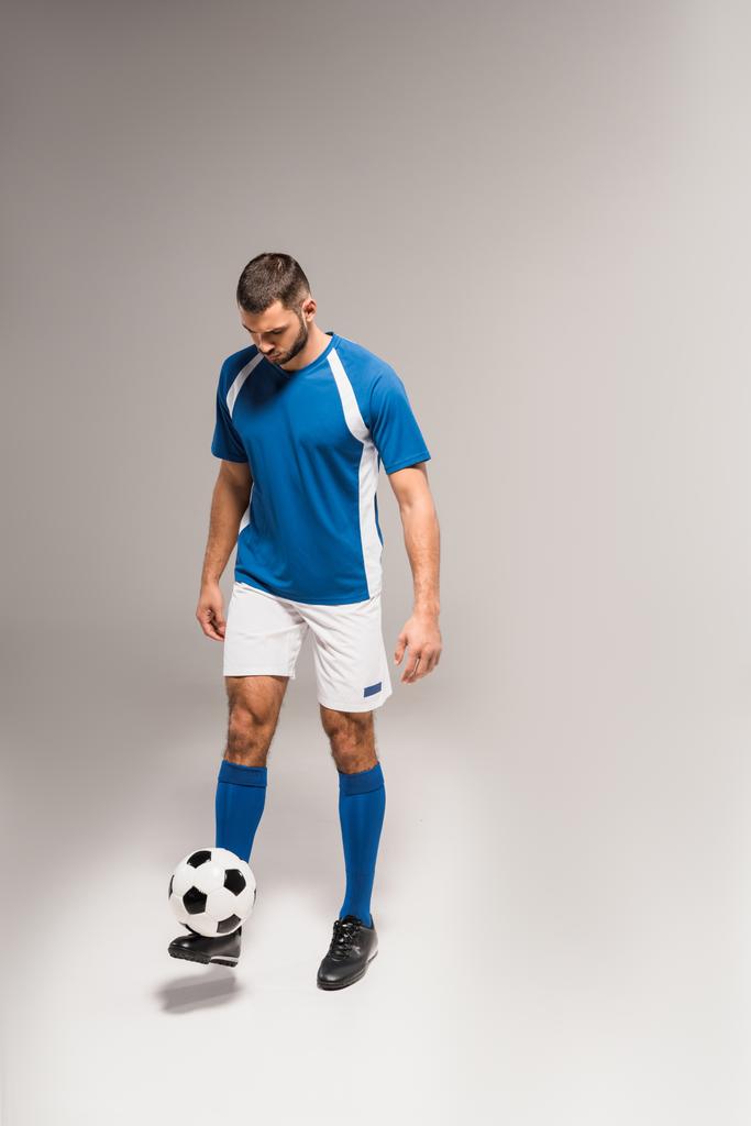 Jovem desportista em sportswear jogar futebol em fundo cinza  - Foto, Imagem