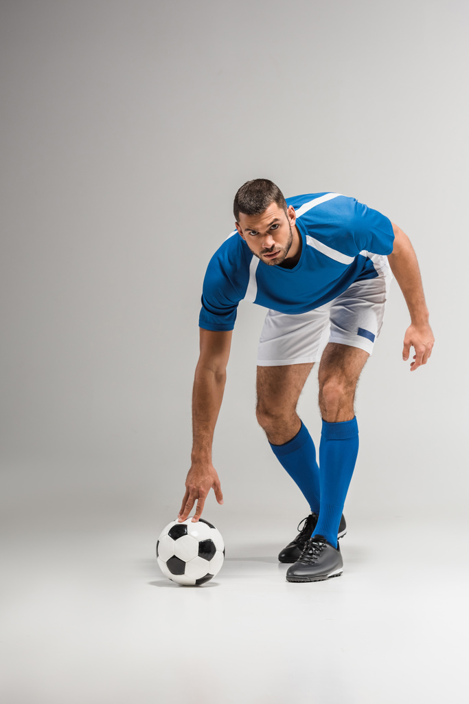 Впевнений спортсмен дивиться на камеру біля футболу на сірому фоні
  - Фото, зображення