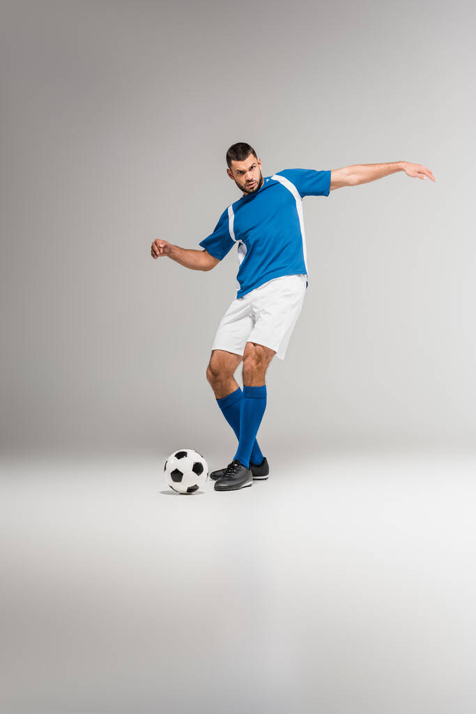 Deportista haciendo ejercicio con fútbol y mirando a la cámara sobre fondo gris  - Foto, Imagen