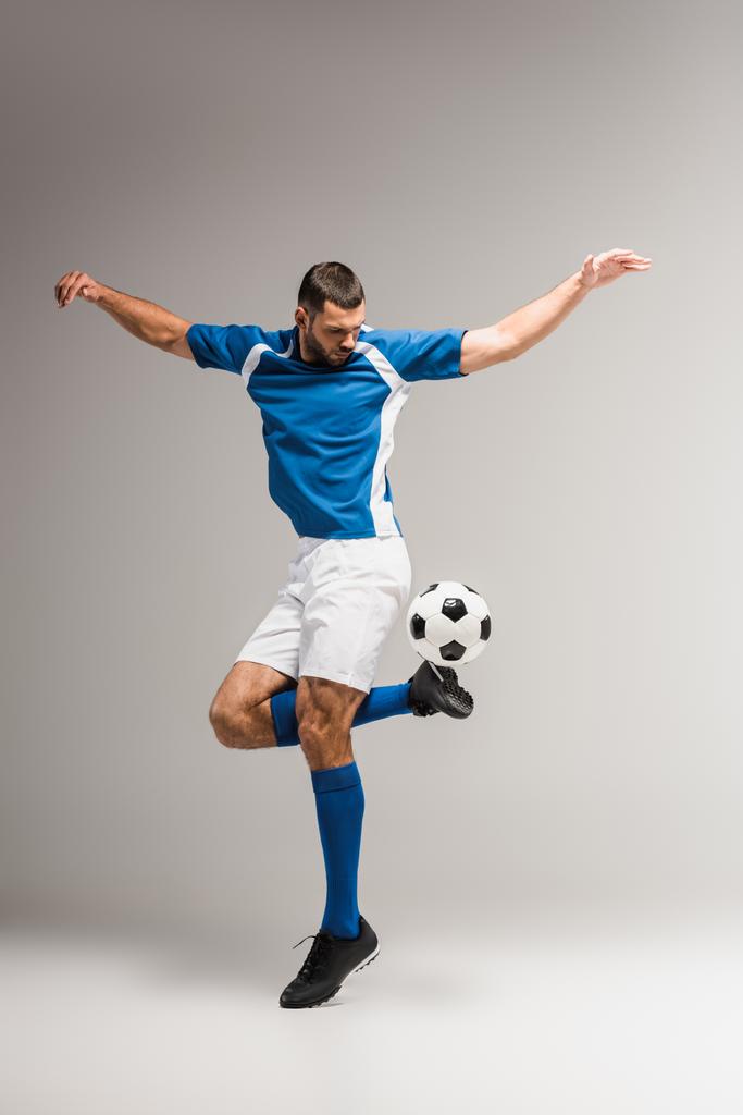 Αθλητικός άνθρωπος άσκηση με το ποδόσφαιρο σε γκρι φόντο  - Φωτογραφία, εικόνα