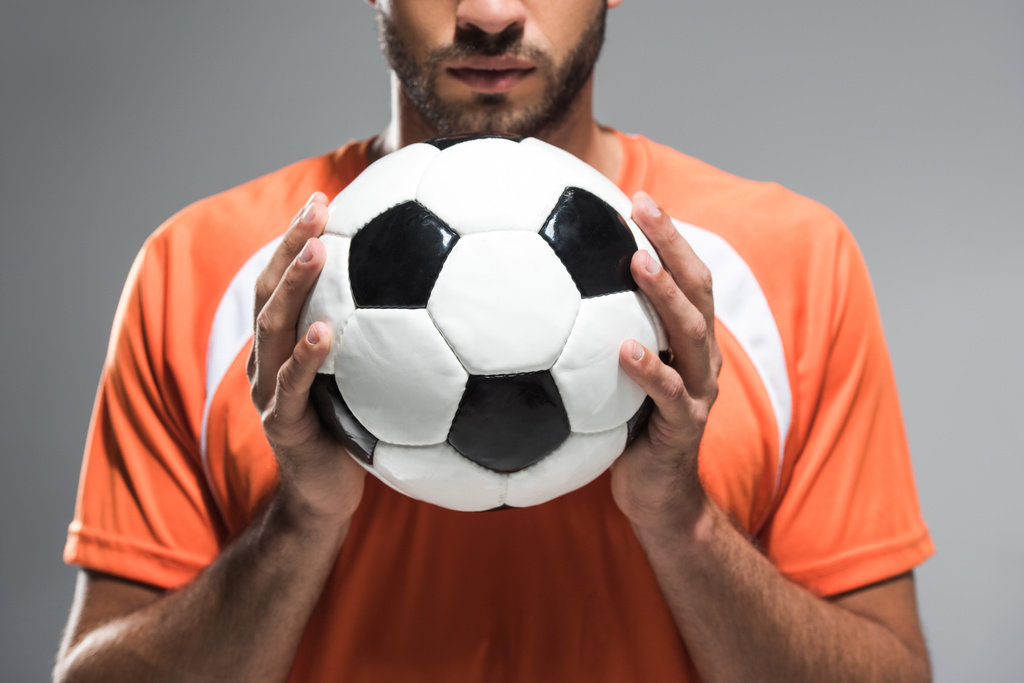 Vista recortada del fútbol en manos de deportista barbudo sobre fondo borroso aislado sobre gris - Foto, imagen