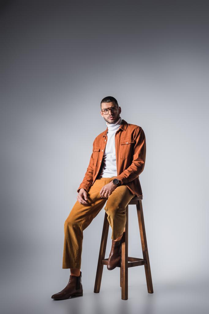 Stylish man looking away on chair on grey background - Photo, Image