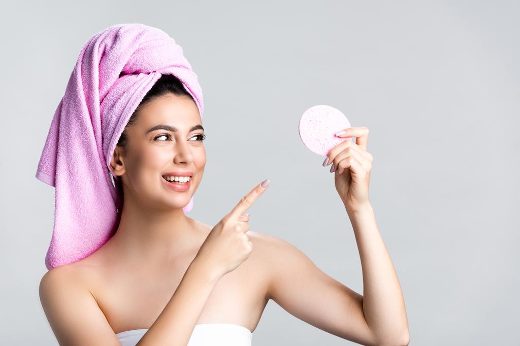 sourire belle femme avec serviette sur les cheveux pointant vers éponge isolée sur gris - Photo, image