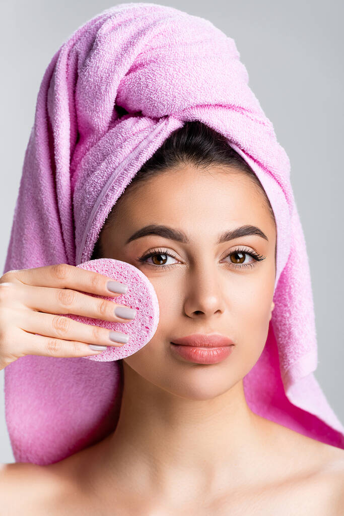 όμορφη γυναίκα με πετσέτα στα μαλλιά χρησιμοποιώντας σφουγγάρι στο πρόσωπο απομονώνονται σε γκρι - Φωτογραφία, εικόνα