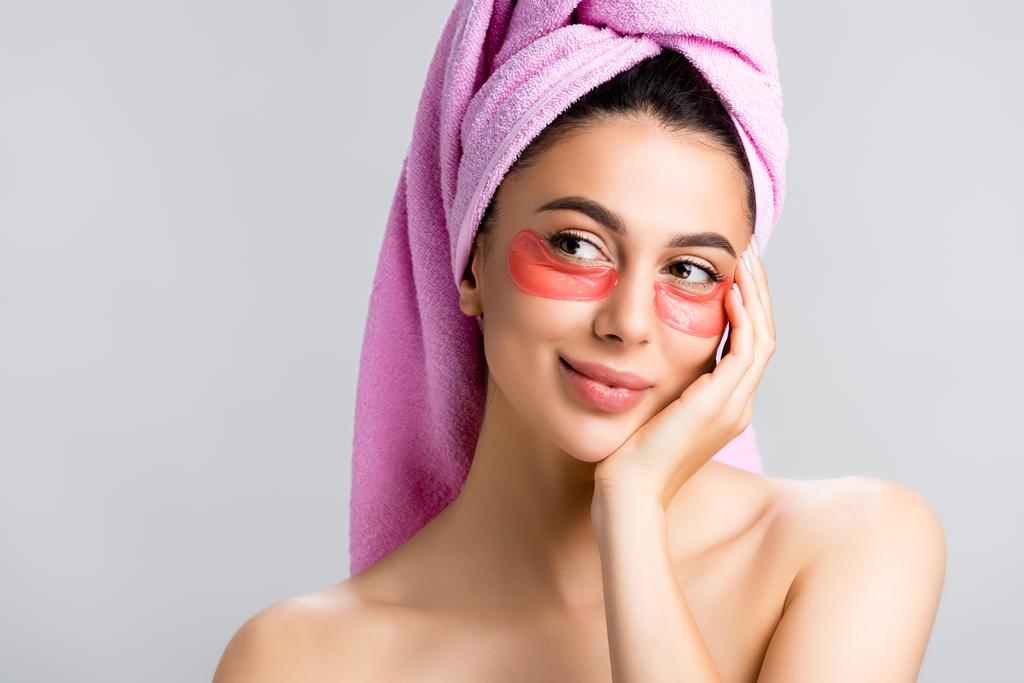 zasněná krásná žena s ručníkem na vlasech a hydrogel oční náplasti na tváři izolované na šedé - Fotografie, Obrázek