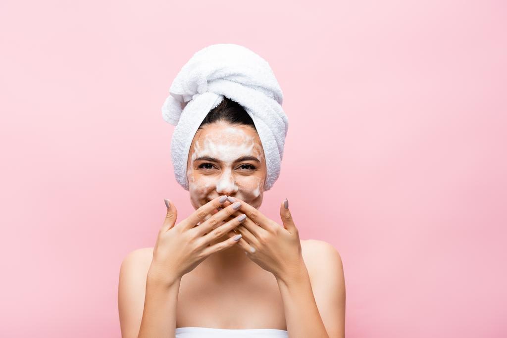 γελώντας όμορφη γυναίκα με πετσέτα στα μαλλιά και αφρό στο πρόσωπο απομονώνονται σε ροζ - Φωτογραφία, εικόνα