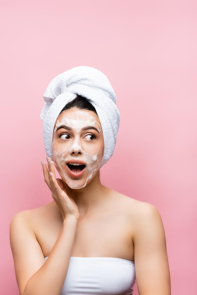shocked beautiful woman with towel on hair and foam on face isolated on pink - Photo, Image