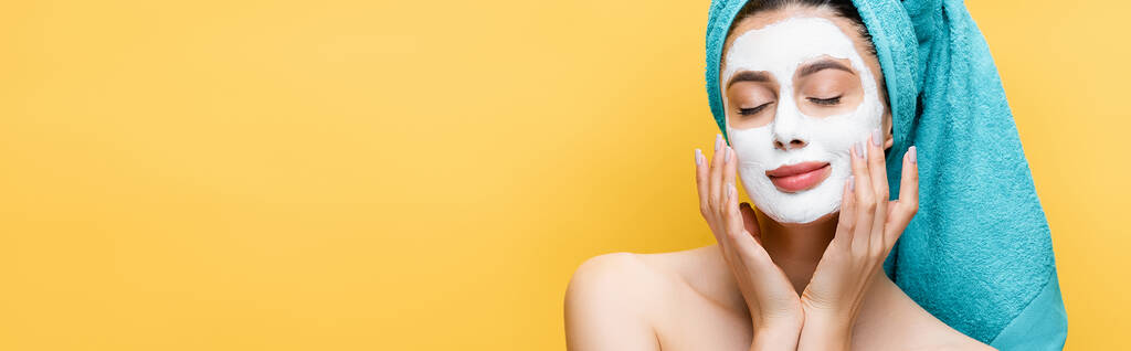 krásná žena se zavřenýma očima, modrý ručník na vlasech a hliněná maska na obličeji izolované na žluté, banner - Fotografie, Obrázek
