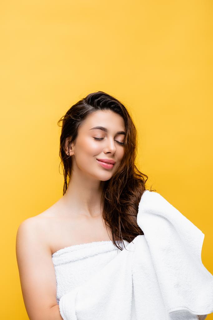 χαμογελαστή όμορφη γυναίκα με βρεγμένα μαλλιά και πετσέτα απομονωμένη στο κίτρινο - Φωτογραφία, εικόνα