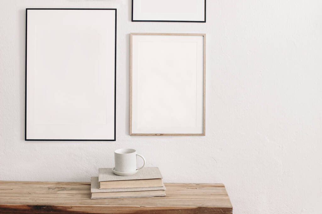Set of black portrait picture frame mockups. Wall art gallery. Cup of coffee on pile of books on old wooden bench, table. White wall background. Scandinavian interior, neutral color palette. - Photo, Image
