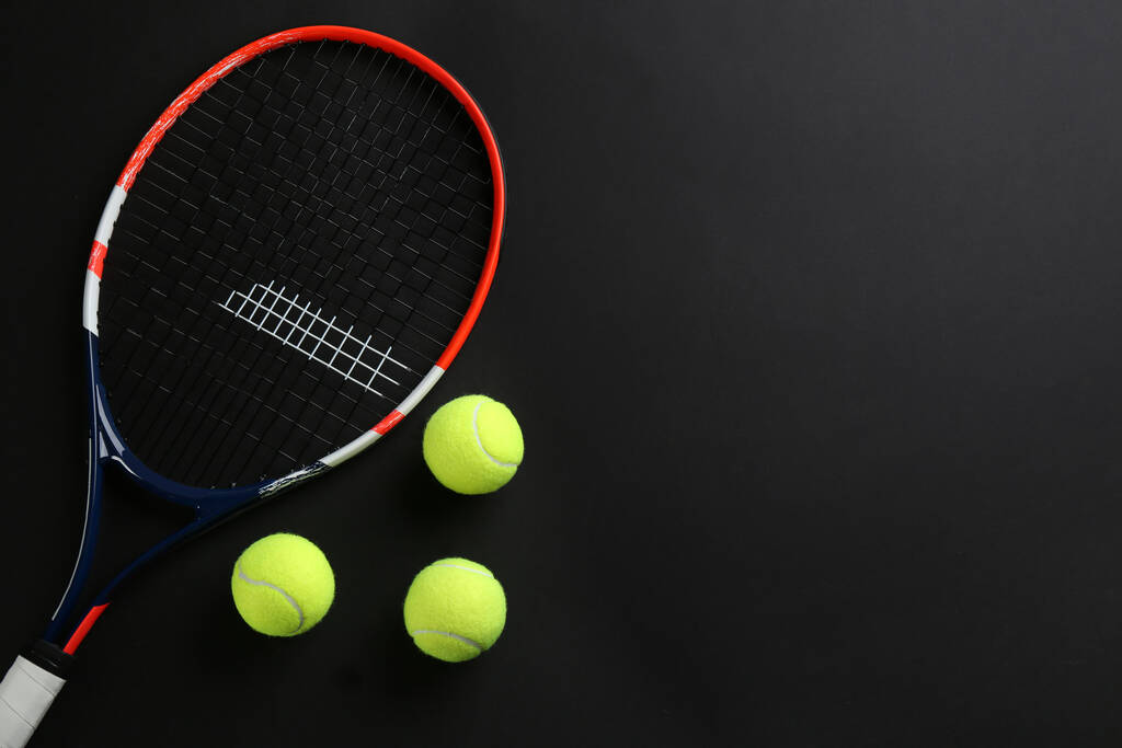 Raqueta de tenis y pelotas sobre fondo negro, suelo plano. Espacio para texto - Foto, imagen