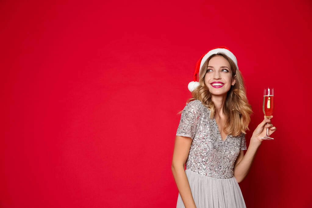 Boldog nő Mikulás kalapban, egy pohár pezsgővel a piros háttéren, hely a szövegnek. Karácsonyi buli - Fotó, kép