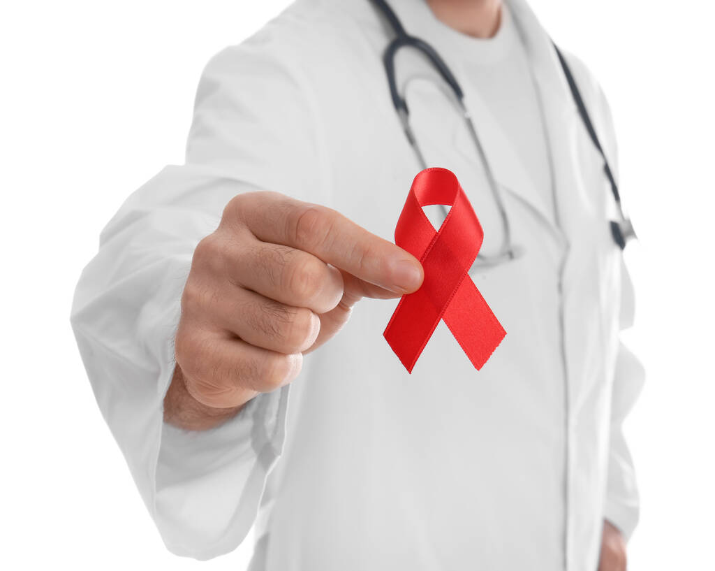 Doctor holding red awareness ribbon on white background, closeup. World AIDS disease day - Photo, Image