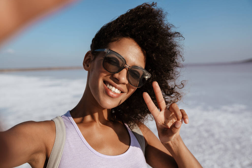 Immagine di felice donna afroamericana gesticolare segno di pace mentre si scattano selfie nella valle del sale - Foto, immagini