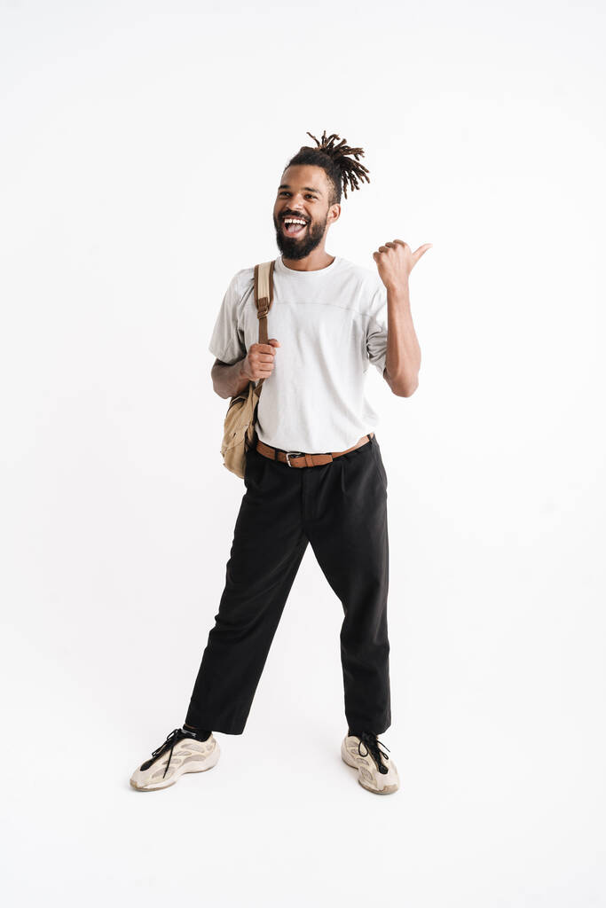 Zdjęcie śmiejącego się african amerykański facet plecak wskazując palec na bok odizolowany na białym tle - Zdjęcie, obraz