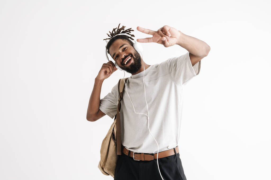 Foto van vrolijke Afrikaans-Amerikaanse man in koptelefoon gebaren vrede teken geïsoleerd over witte muur - Foto, afbeelding