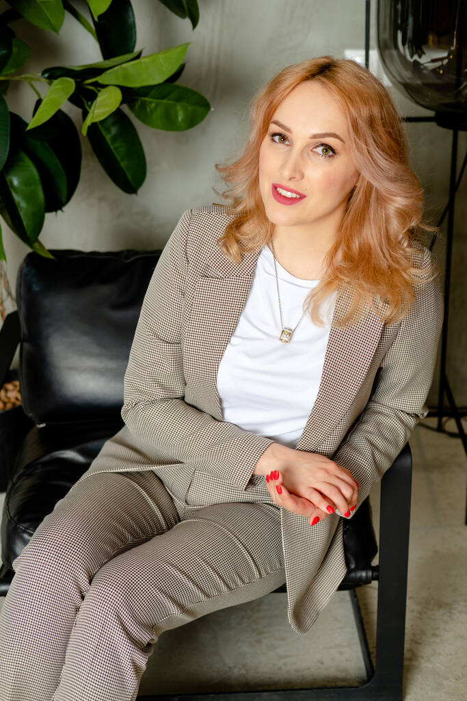 woman sitting on a chair. portrait of a strong businesswoman. The girl in a classic suit in the office. Girl in a loft style office - Photo, Image