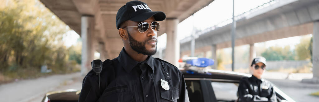 komoly afro-amerikai rendőr néz félre elmosódott kolléga a háttérben a városi utcán, banner - Fotó, kép