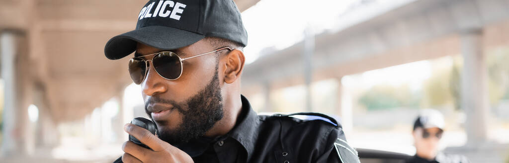 poliziotto afroamericano che parla alla radio vicino alla poliziotta su sfondo sfocato, striscione - Foto, immagini