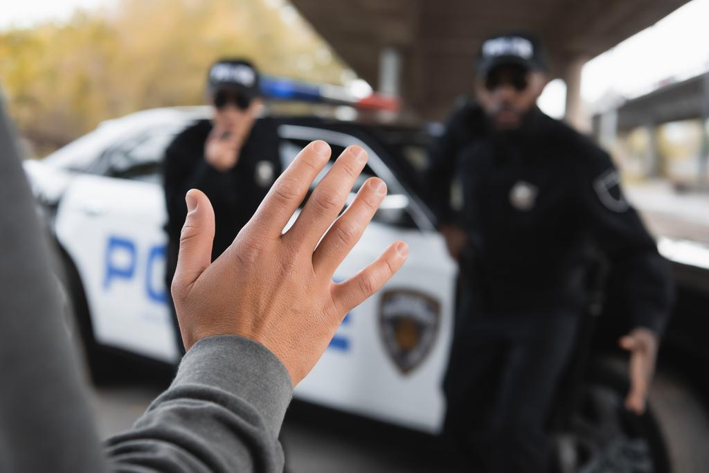 delincuente mostrando la mano con oficiales de policía multiculturales borrosas en el fondo al aire libre - Foto, imagen