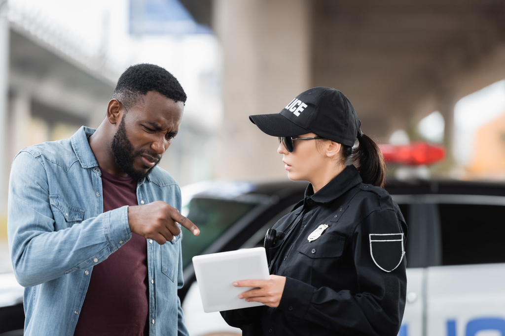 preocupado afro-americano vítima apontando com o dedo para tablet em mãos de policial no fundo borrado ao ar livre - Foto, Imagem