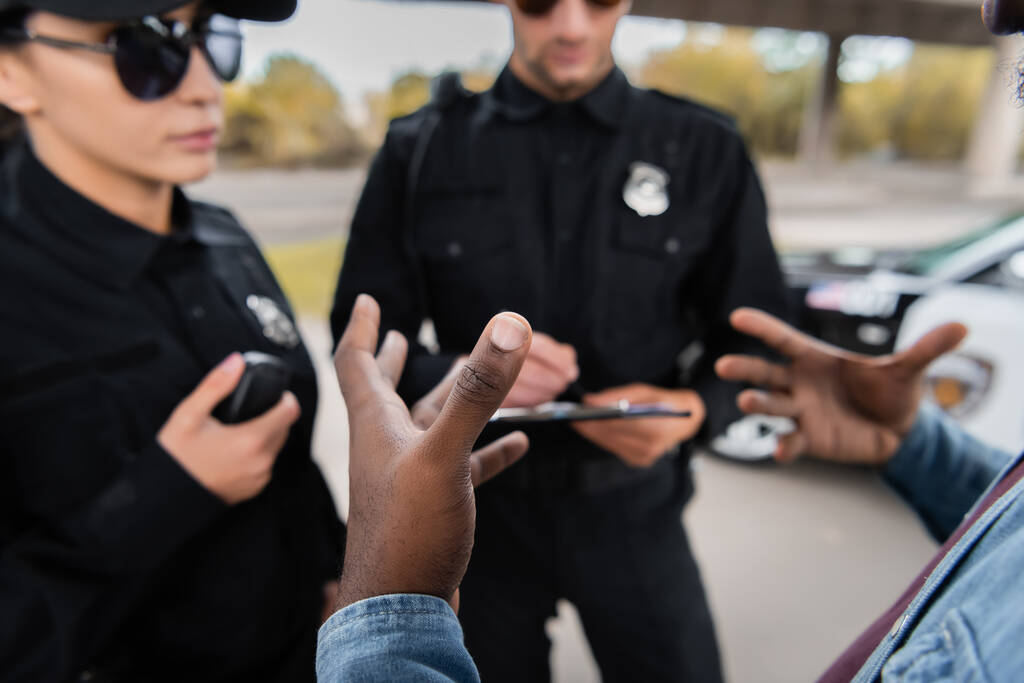 Afro-Amerikan erkek kurban, arka planda bulanık bir şekilde polis memurlarının yanında el kol hareketi yapıyor.  - Fotoğraf, Görsel