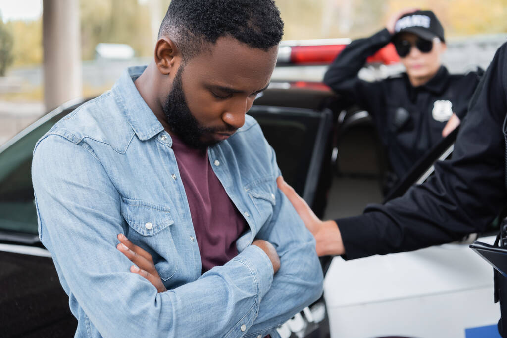 Triste afro-americana vítima de pé perto de policial e carro ao ar livre  - Foto, Imagem