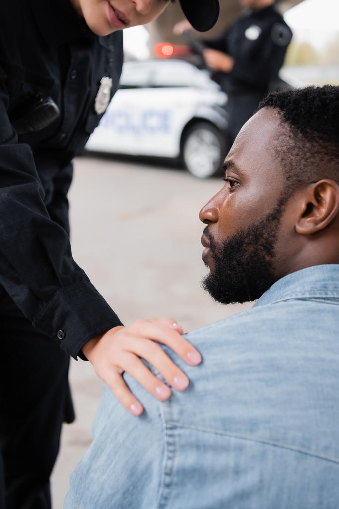 Африканская американская жертва смотрит в сторону офицера полиции на размытом фоне на открытом воздухе  - Фото, изображение