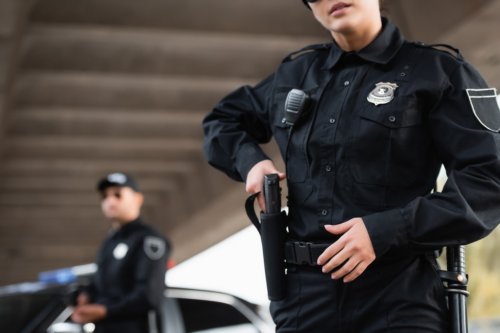 Поліцейська взяла зброю з кобури біля колеги на розмитому тлі
  - Фото, зображення