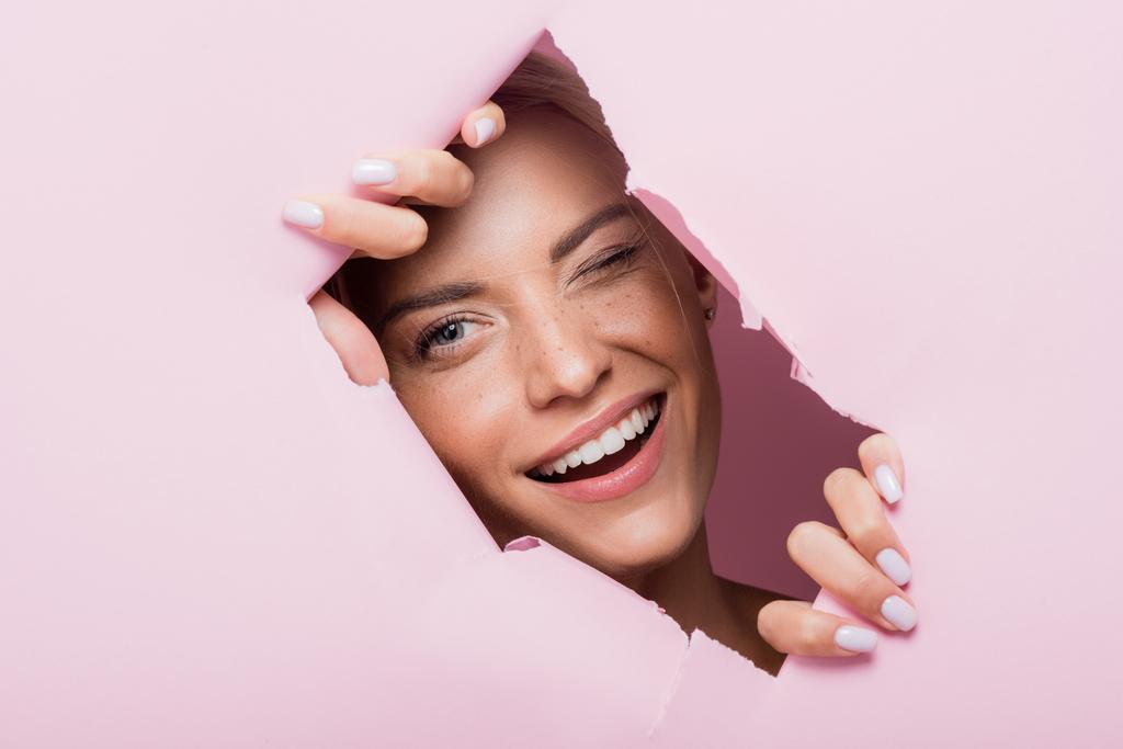 lächelnde schöne Frau mit Sommersprossen im rosa Papierloch - Foto, Bild