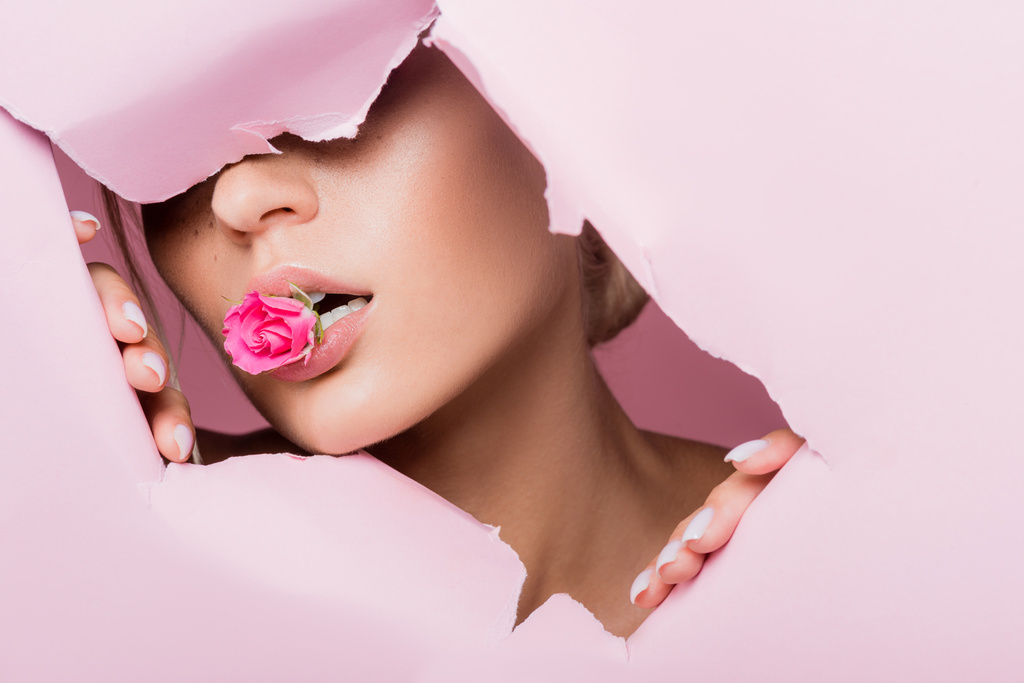 όμορφη γυναίκα με τριαντάφυλλο στο στόμα σε ροζ χάρτινη τρύπα - Φωτογραφία, εικόνα