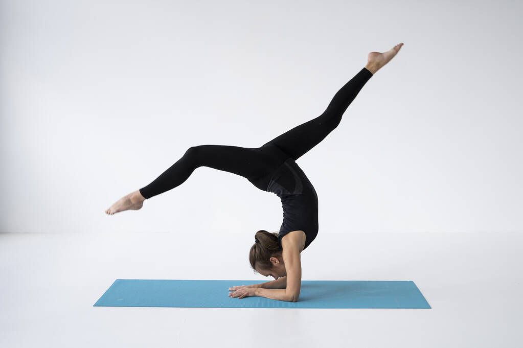 Młoda kobieta ćwiczy jogę w studio. Szczupła młoda dziewczyna w czarnym stroju sportowym ćwiczy jogę na niebieskiej macie. Pojęcie zdrowego życia i naturalnej równowagi pomiędzy rozwojem ciała i umysłu. - Zdjęcie, obraz