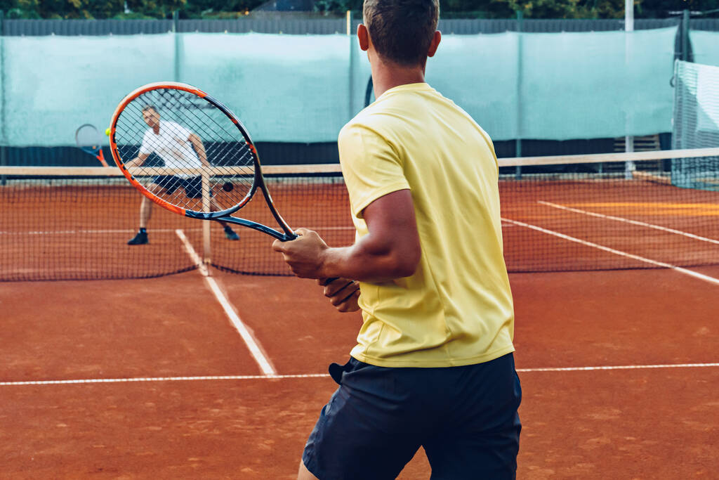 Двоє чоловіків грають у теніс на глиняному тенісному полі
 - Фото, зображення