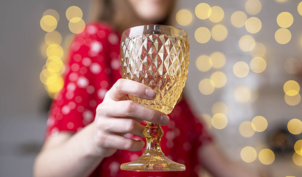 Женщина дома украшена к Рождеству держа бокал вина и ура близко. - Фото, изображение