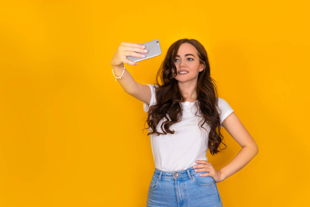 beautiful brunette girl makes selfie on a yellow background - Photo, Image