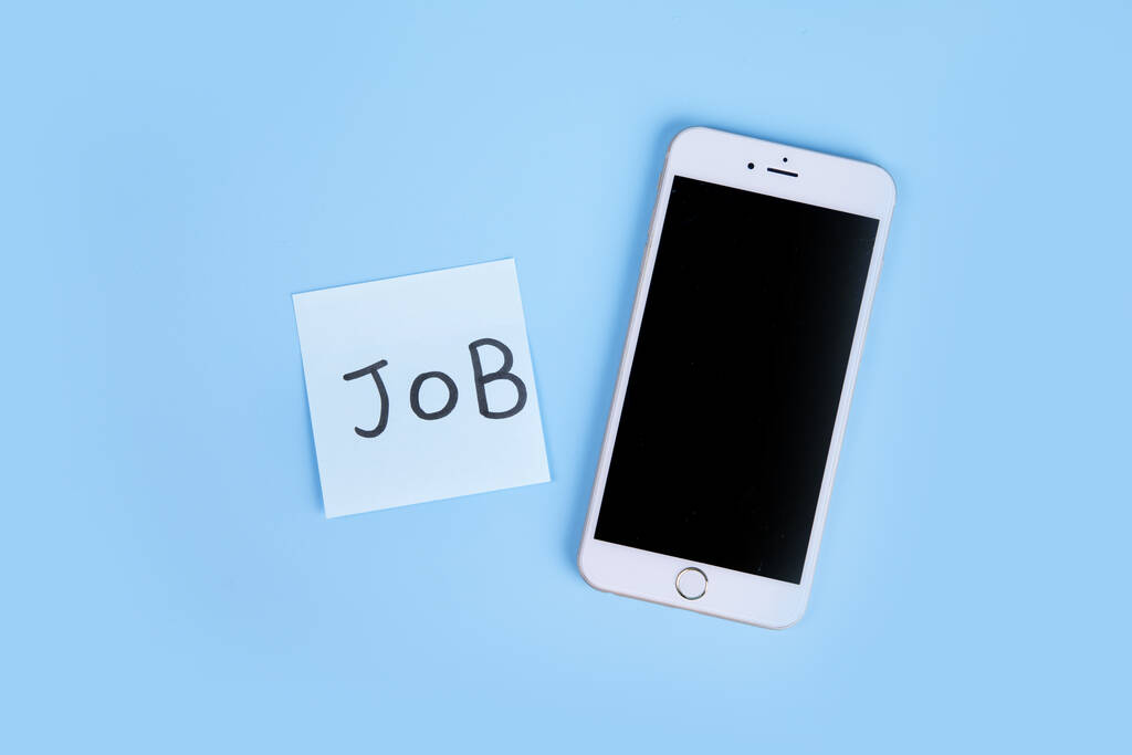 Une vue de dessus d'une note collante avec du texte Job et un téléphone sur une surface bleue - Photo, image