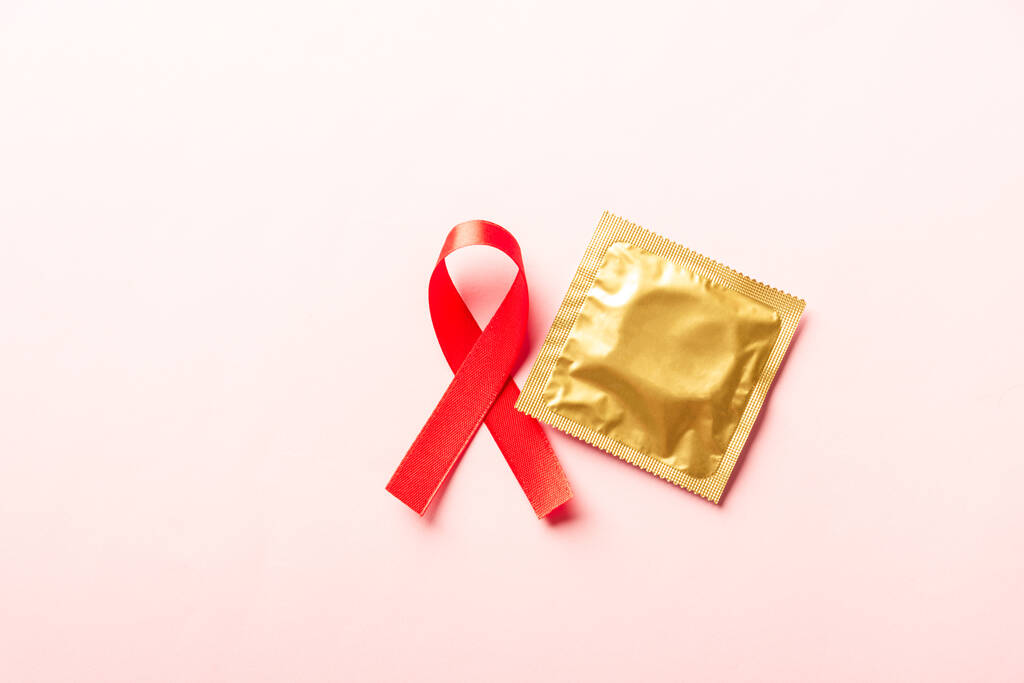 Fiocco rosso simbolo HIV, AIDS cancro consapevolezza e preservativo con ombre, studio girato isolato su sfondo rosa, Medicina sanitaria sessualmente concetto, Giornata Mondiale dell'AIDS - Foto, immagini