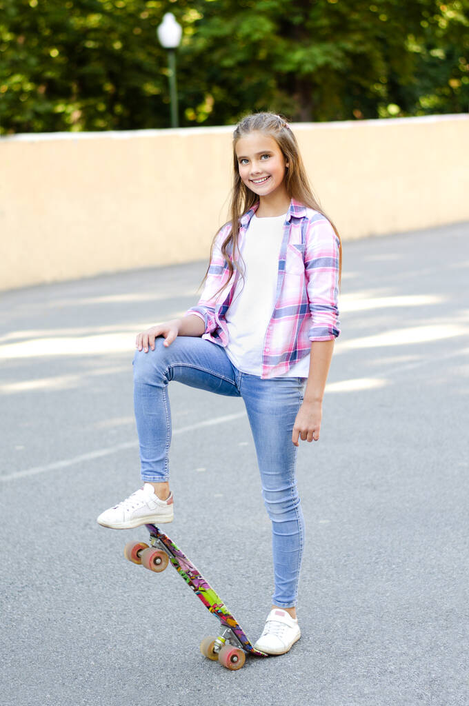 スケートボードに座ってかわいい女の子の子供を笑顔。屋外で夏の日にペニーボードでプレティーン - 写真・画像