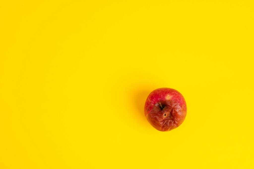 Gammeliger Apfel mit Wurm auf gleichmäßigem gelben Hintergrund. - Foto, Bild