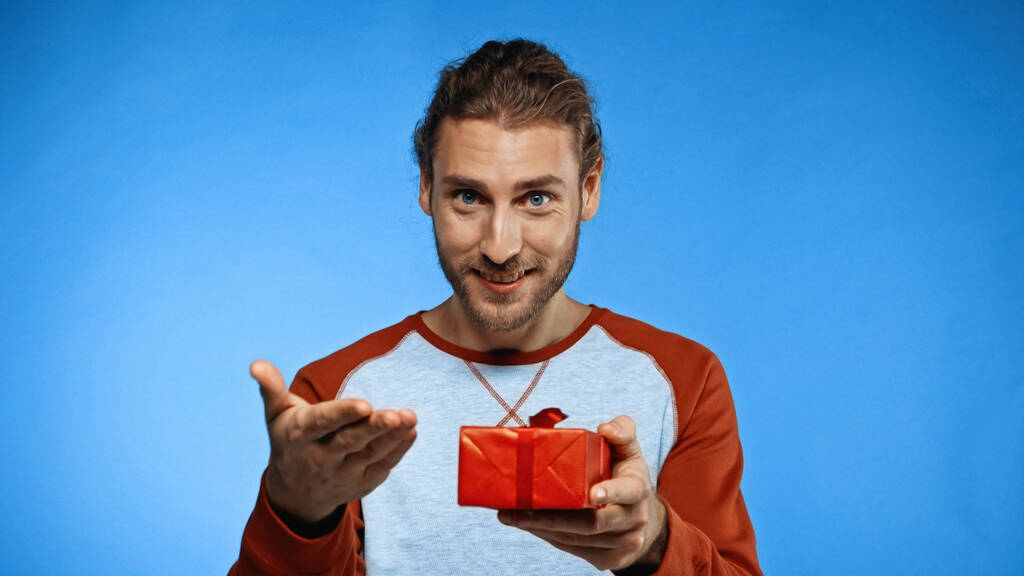 šťastný vousatý muž drží zabalený dárek a ukazuje rukou na modré - Fotografie, Obrázek