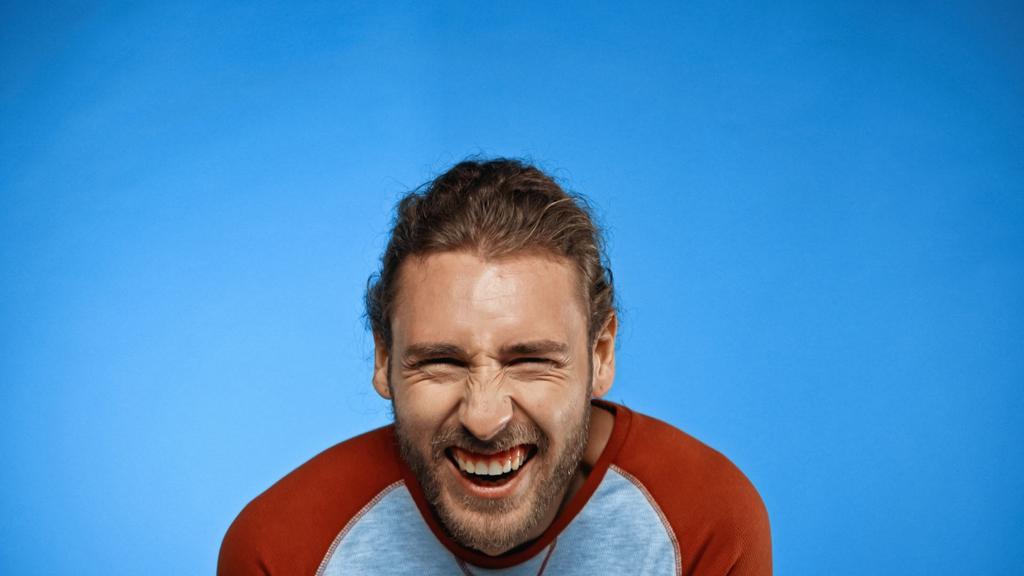 бородатый молодой человек смотрит в камеру и смеется над синим - Фото, изображение