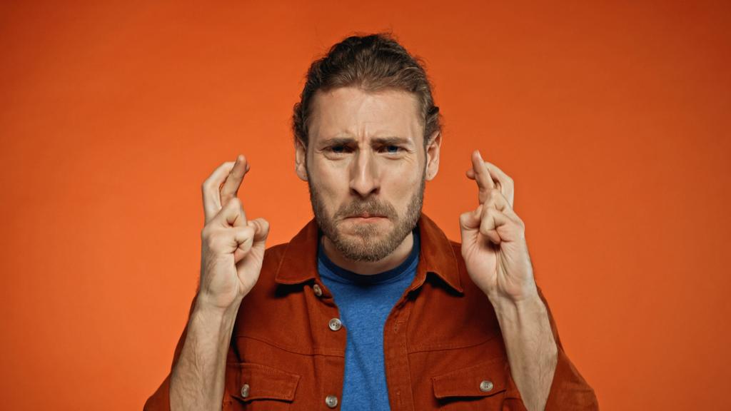 joven barbudo con los dedos cruzados en naranja  - Foto, Imagen