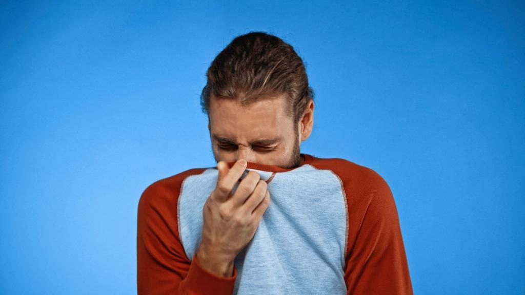giovane uomo che copre il naso con la camicia mentre si sente odore sgradevole sul blu - Foto, immagini