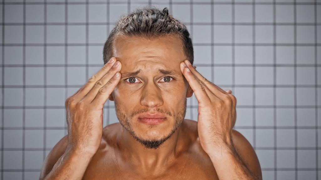 hombre barbudo mirando a la cámara y tocando arrugas en el baño  - Foto, Imagen