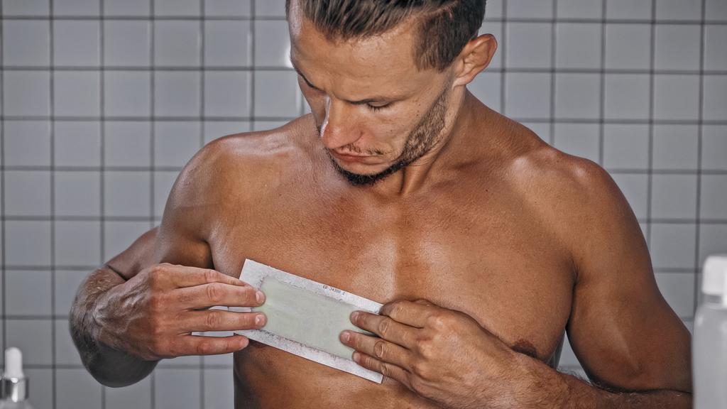 parrakas mies soveltamalla vaha nauhat rinnassa kylpyhuoneessa  - Valokuva, kuva