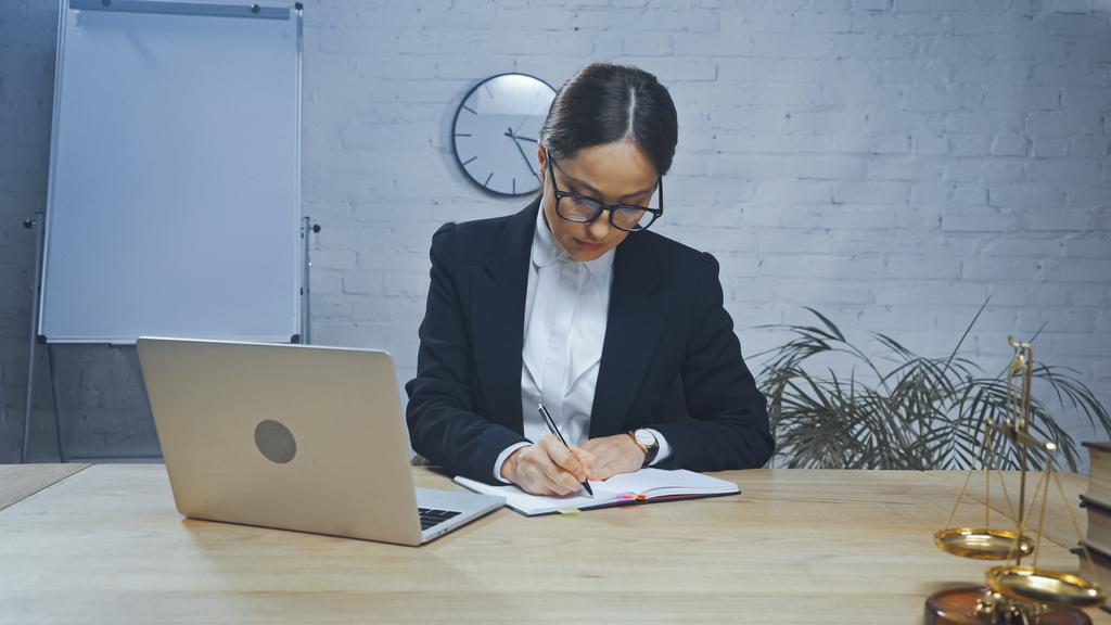 Agente de seguros escribiendo en el portátil cerca de la computadora portátil y escalas en primer plano borrosa  - Foto, imagen