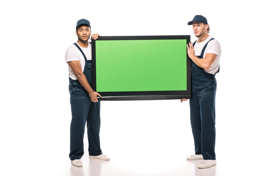 full length of shocked multicultural movers carrying plasma tv with green screen on white - Photo, Image