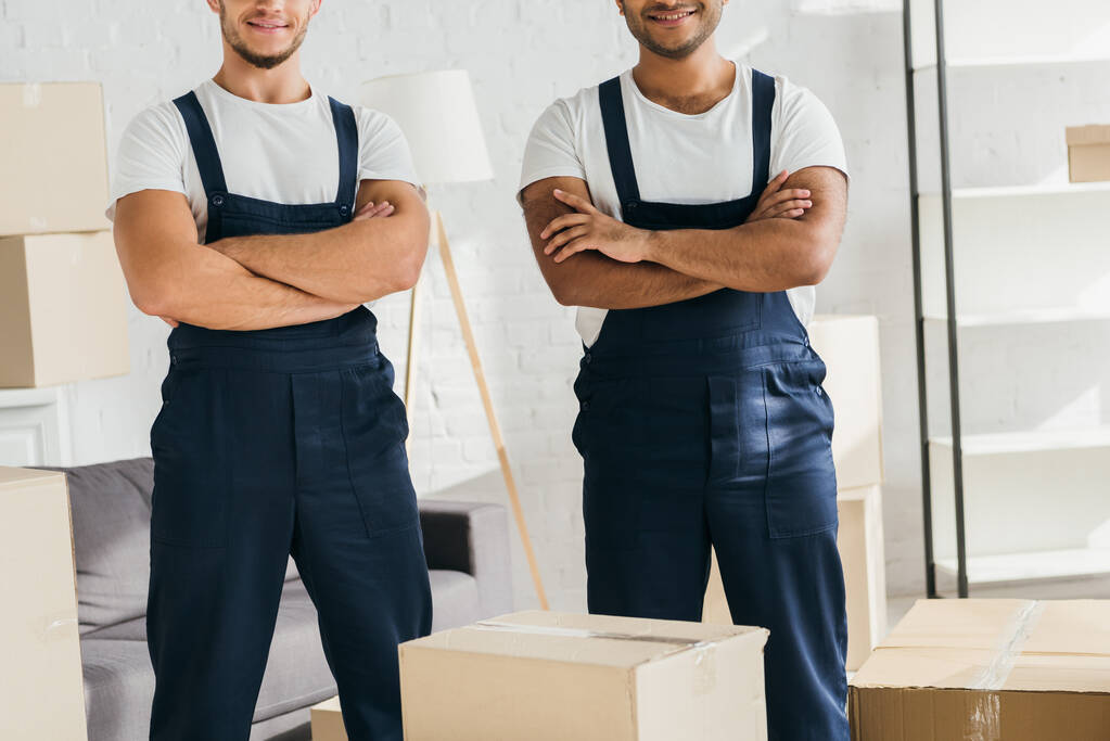 cropped view of multicultural movers standing with crossed arms near boxes  - Photo, Image