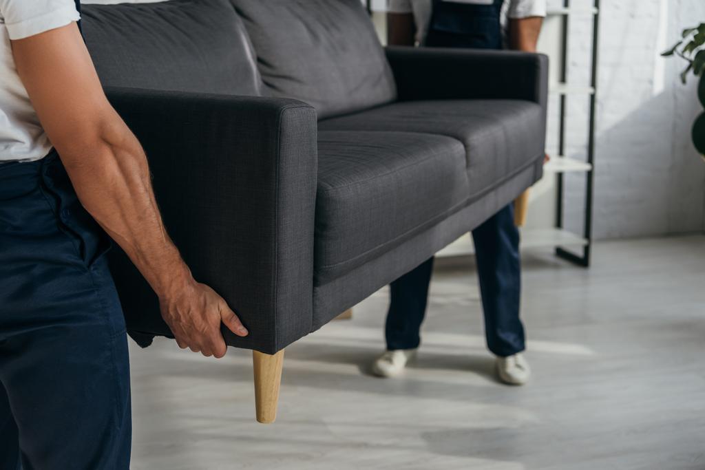 Teilansicht von Arbeitern, die schweres Sofa in Wohnung tragen  - Foto, Bild