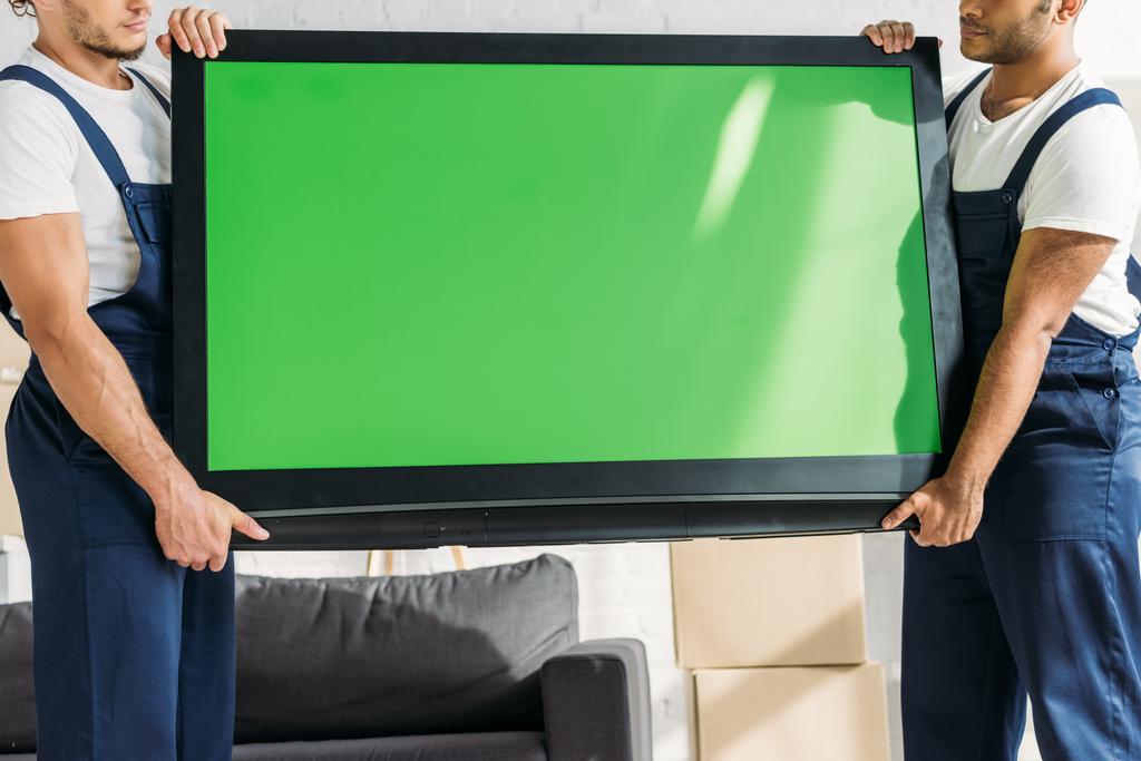 kivágott kilátás multikulturális mozgó egyenruhás szállító plazma tv zöld képernyős lakásban  - Fotó, kép
